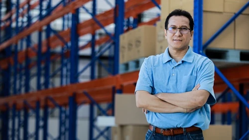 Man standing with arms crossed in front of storage shelves filled with boxes